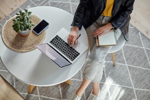 Jovem mulher usando laptop e fazendo anotações no notebook sentada no local de trabalho em casa trabalho remoto v