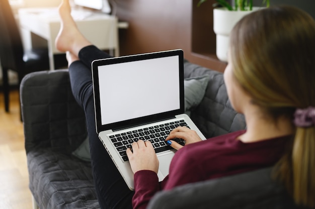 Jovem mulher usando laptop enquanto está sentado no sofá confortável, interior de casa. Ficar em casa. Foto de alta qualidade