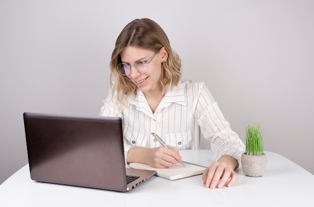 Jovem mulher usando laptop, sorrindo e escrevendo algo em um caderno