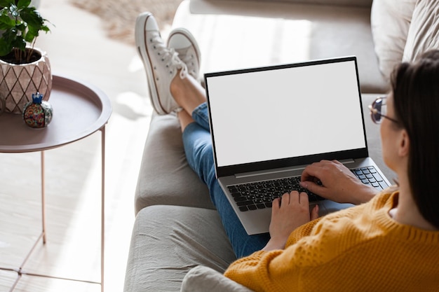 Jovem mulher usando maquete em branco de tela de laptop deitada no sofá em casa