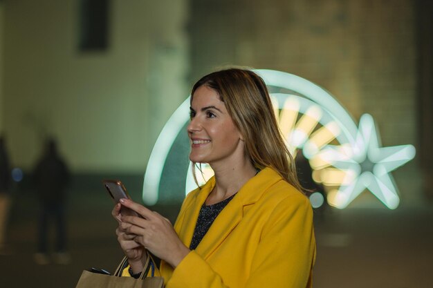 Jovem mulher usando seu smartphone desfrutando de um passeio na cidade com as luzes de Natal