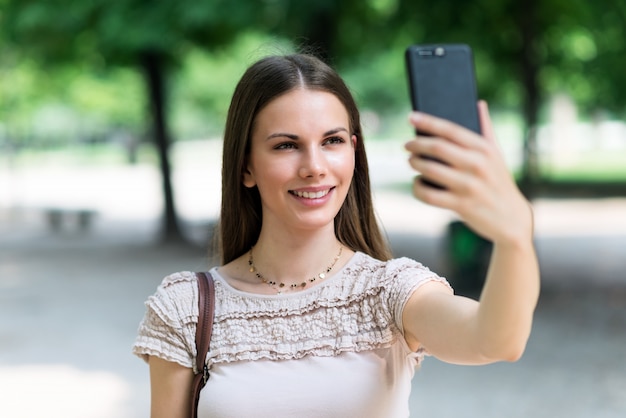 Jovem, mulher, usando seu telefone celular para tirar uma foto