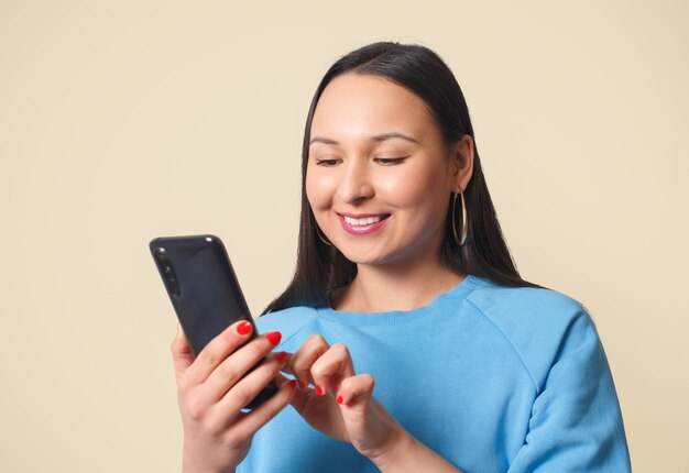 Jovem mulher usando smartphone e sorrindo. Sobre um fundo creme.