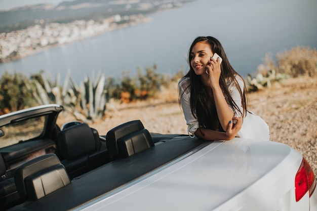 Jovem mulher usando telefone celular e aguardando carro conversível em um dia quente de verão