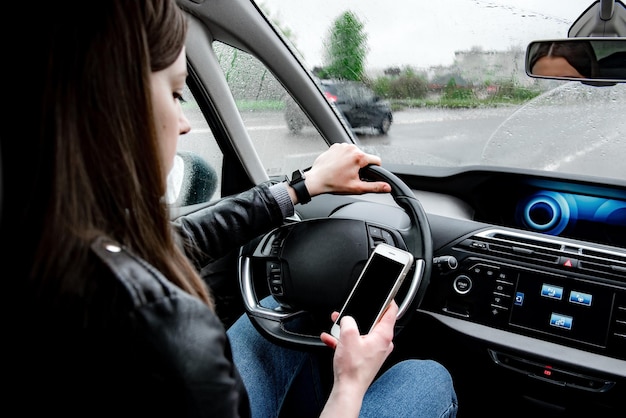 Jovem mulher usando telefone celular enquanto dirigia o carro em condições de mau tempo.