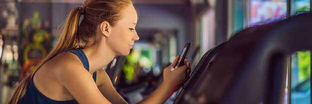 Jovem mulher usando telefone enquanto treinava na academia mulher sentada na máquina de exercícios segurando o celular