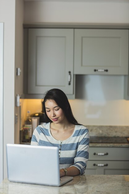 Jovem mulher usando um laptop na cozinha