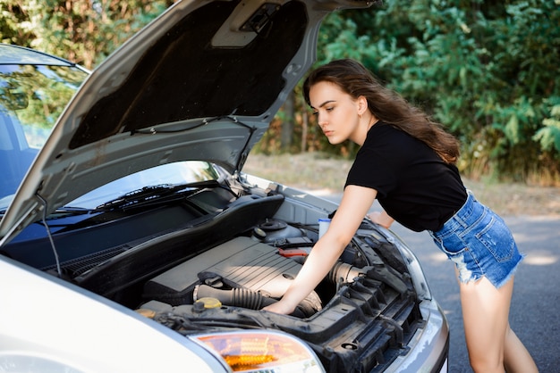 Jovem mulher verifica o motor do carro e tenta reparar o carro sozinha.