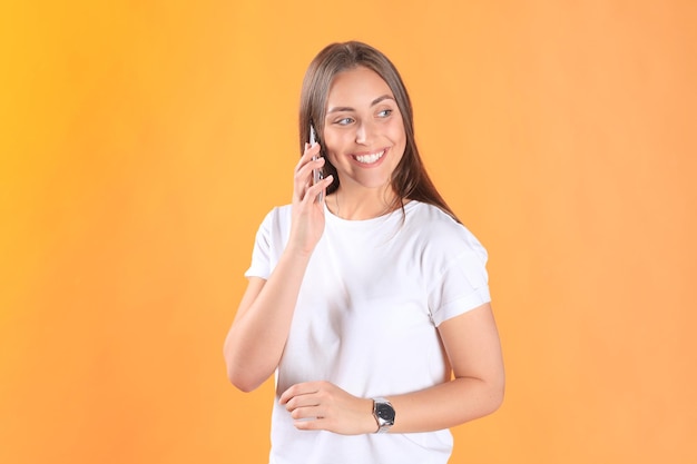 Jovem mulher vestida com roupas básicas isoladas em fundo amarelo, usando telefone celular.