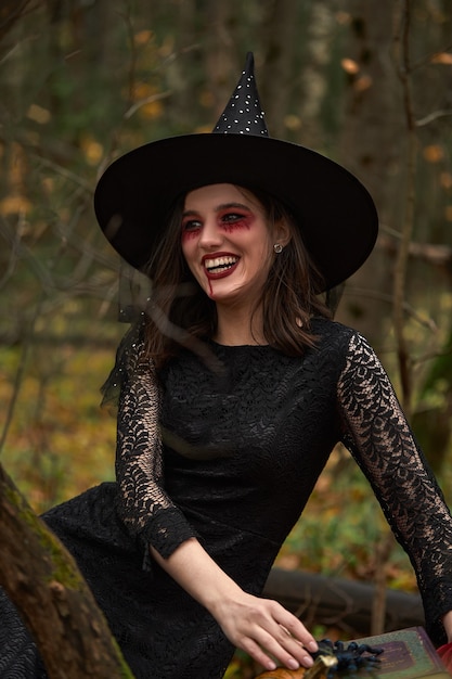 Jovem mulher vestida de preto com chapéu de bruxa e abóbora laranja colocada ao redor da floresta, o conceito de halloween. tema de terror.