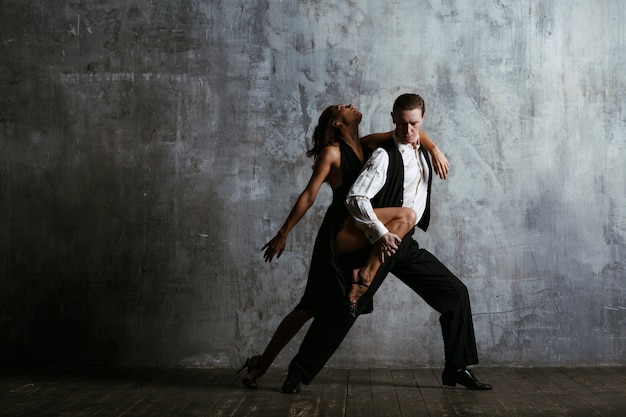 Jovem mulher vestida de preto e homem dança tango