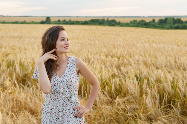 Jovem mulher vestida num campo de trigo de verão. Menina sorridente no Prado Dourado. Liberdade