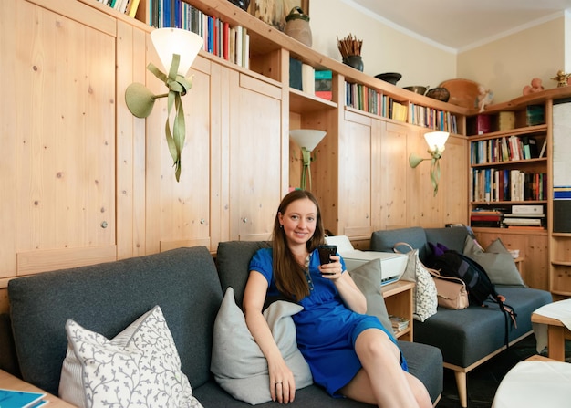 Jovem mulher vestindo vestido sentado e bebendo chá ou café no sofá no café do lobby do hotel. Senhora em seus 30 anos aproveite a vida. Garota sorridente feliz sente-se. Pessoa do sexo feminino, retrato de senhora caucasiana no restaurante.