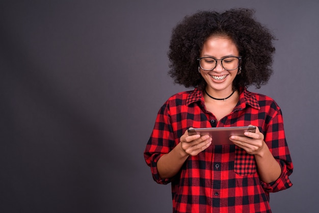 Jovem multiétnica afro-americana hipster com cabelo afro contra uma parede cinza