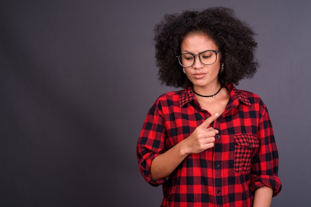 Jovem multiétnica afro-americana hipster com cabelo afro contra uma parede cinza