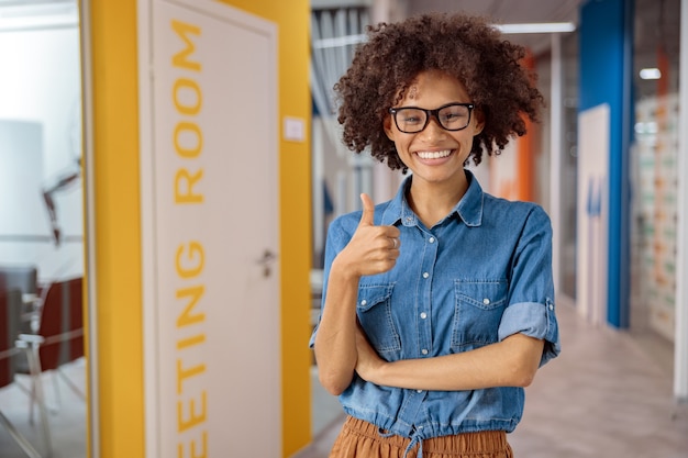 Jovem multiétnica segurando o polegar em coworking