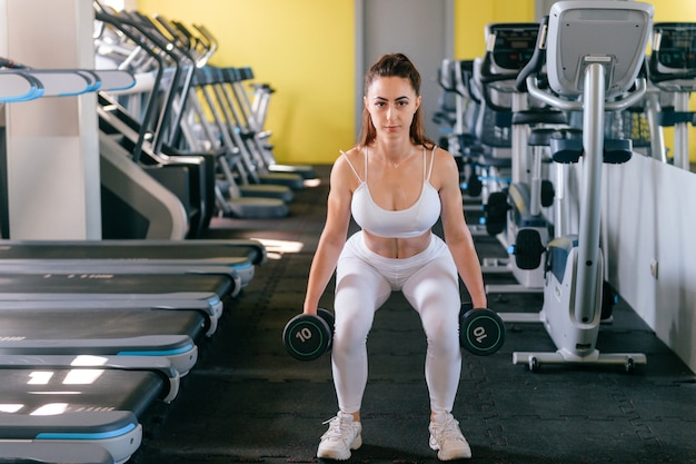 Jovem muscular com corpo bonito, fazendo exercícios com halteres