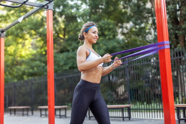Jovem musculosa treina músculos com elásticos de fitness em um campo de treino esportivo Estilo de vida saudável Fitness e musculação Treinamento de resistência