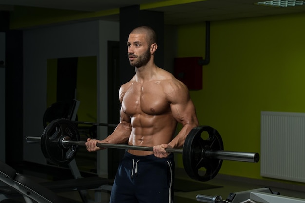 Jovem musculoso fazendo exercícios de peso pesado para bíceps na academia