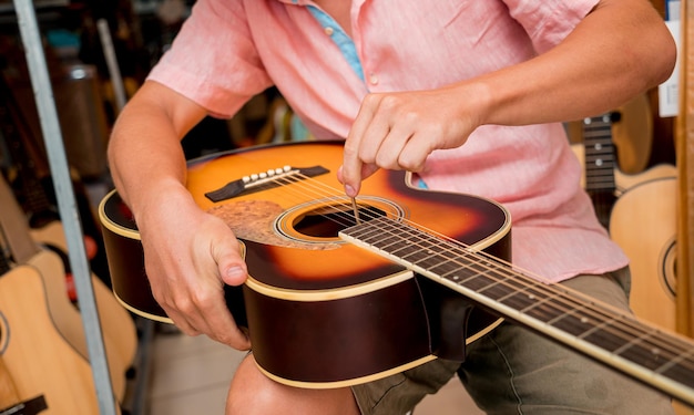 Jovem músico afinando uma guitarra clássica em uma loja de guitarra