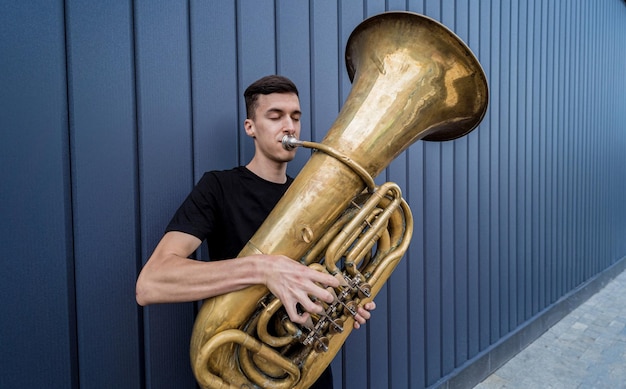 Jovem músico de rua tocando tuba perto da grande parede azul