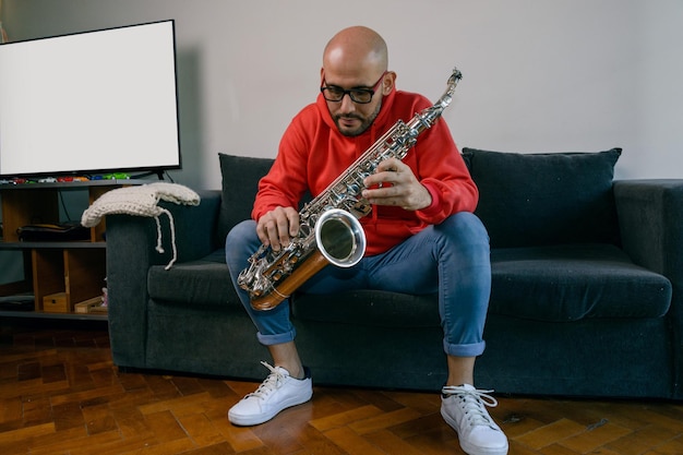 jovem músico latino estudando em casa segura seu saxofone e está pensando em como fazer o acorde