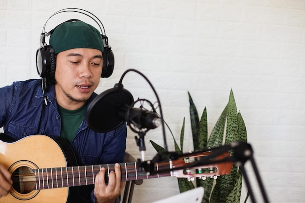 Jovem músico masculino está tocando violão e cantando uma música, gravando videoclipe para transmissão ao vivo