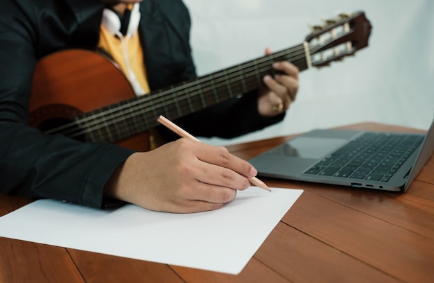 Jovem músico segurando um lápis para fazer anotações em uma aula de música, aprender violão online com um laptop