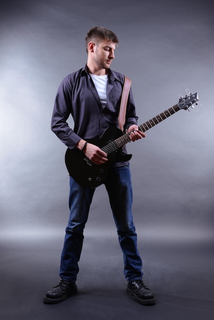 Jovem músico tocando guitarra em fundo cinza