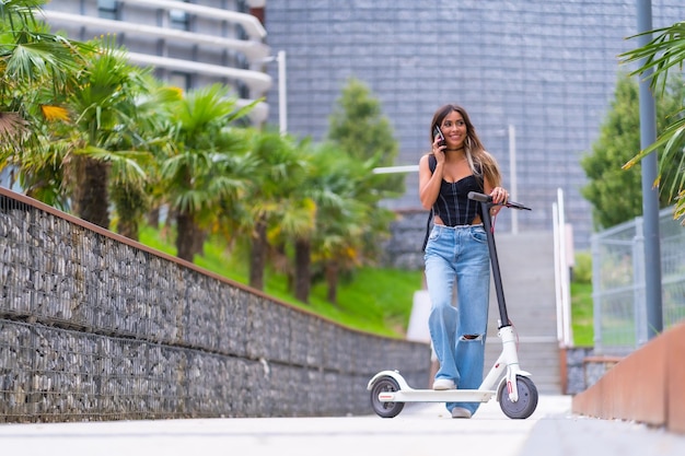 Jovem na cidade com uma scooter elétrica falando ao telefone transporte sustentável