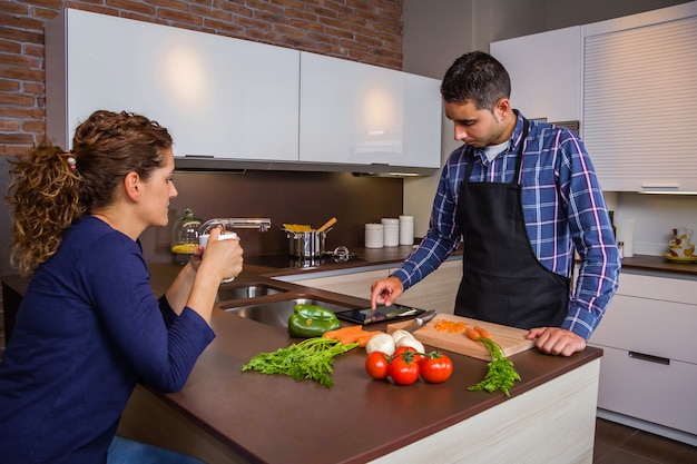 Jovem na cozinha de casa preparando comida e procurando receita em um tablet eletrônico. conceito moderno de estilo de vida familiar.