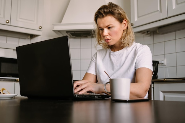 Jovem na cozinha trabalhando no computador