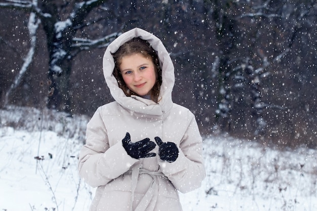 Jovem na floresta de inverno durante uma nevasca. Retrato de uma jovem feliz na floresta de inverno