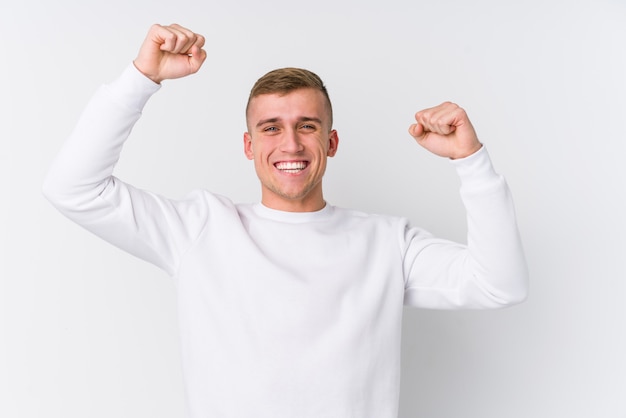 Jovem na parede branca, comemorando um dia especial, pula e levanta os braços com energia