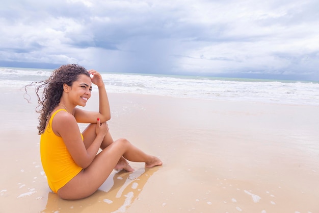 Jovem na praia Afro mulher sentada na areia da praia em um lindo dia de verão