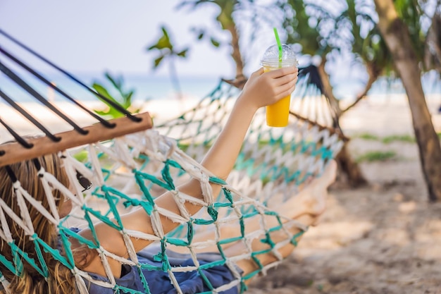 Jovem na praia em uma rede com uma bebida