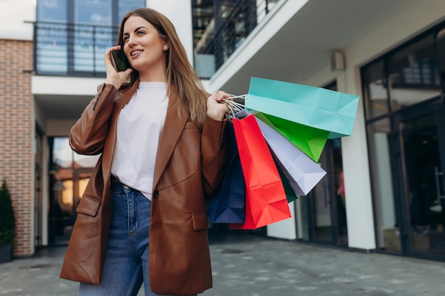 Jovem na rua com sacos coloridos falando ao celular