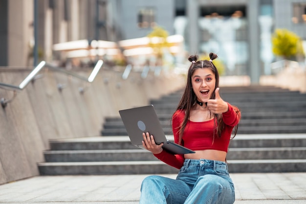 Jovem na rua usando laptop e mostra como