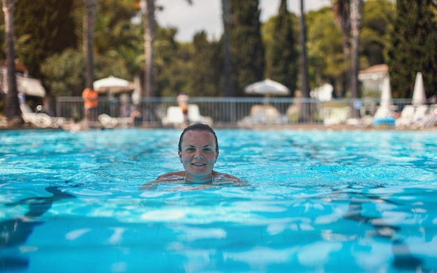 Jovem nadando em direção à câmera na piscina vazia do resort tropical, sorrindo