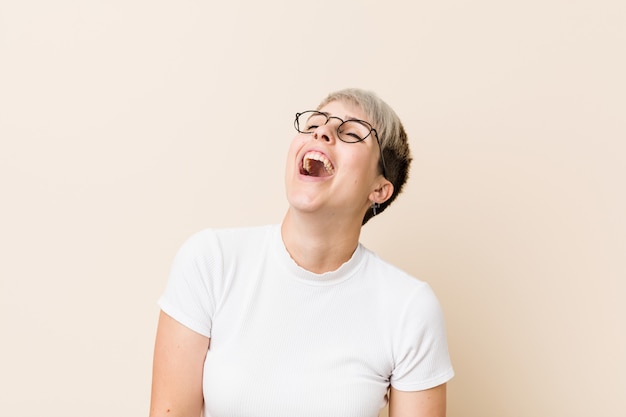 Jovem natural autêntica mulher vestindo uma camisa branca relaxada e feliz rindo, pescoço esticado, mostrando os dentes.