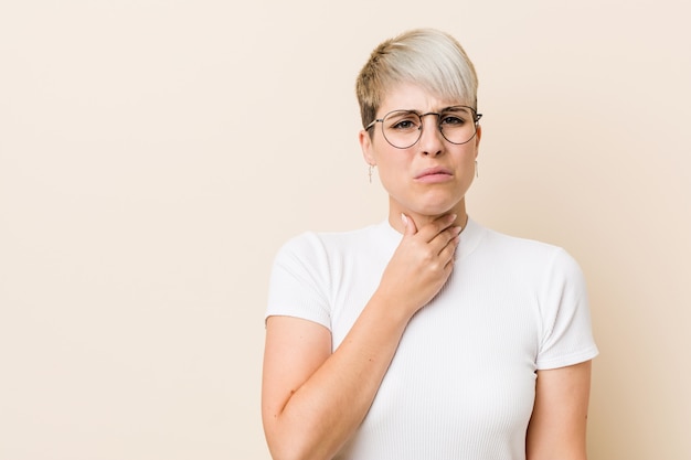 Jovem natural autêntica mulher vestindo uma camisa branca sofre dor na garganta devido a um vírus ou infecção.