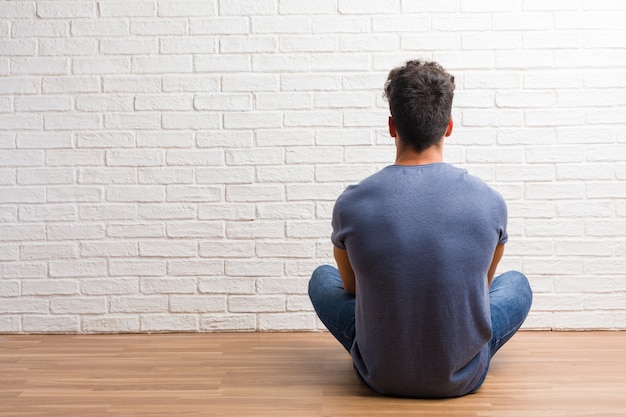 Jovem natural sente-se em um piso de madeira, mostrando de volta, posando e esperando, olhando para trás