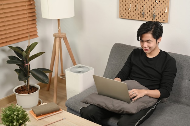 Jovem navegando na internet com o laptop no sofá.