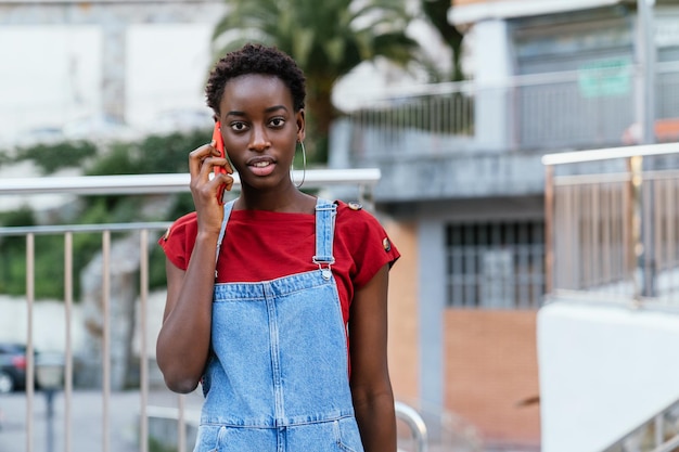 Jovem negra africana falando no celular andando por uma rua da cidade olhando para a câmera