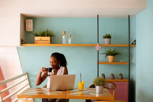 Jovem negra bebendo café enquanto trabalhava no laptop no café