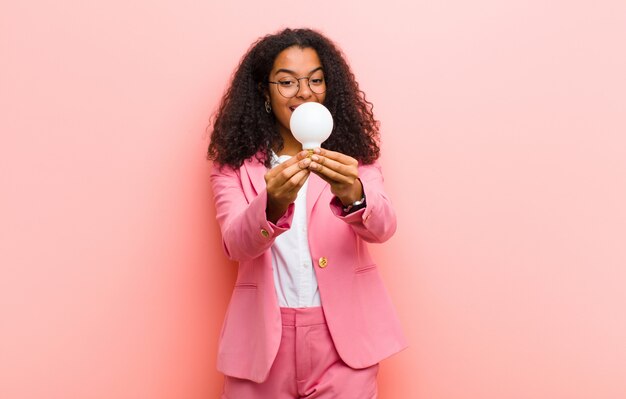 Jovem negra bonita com uma lâmpada tendo uma ideia contra uma parede rosa