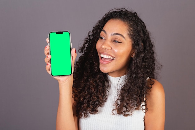 Jovem negra brasileira segurando celular e mostrando foto de publicidade na tela