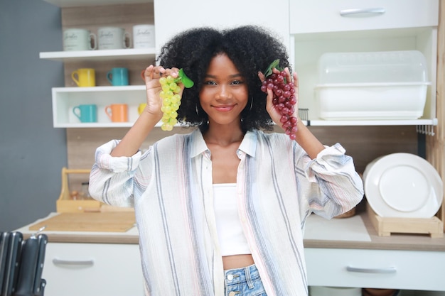 Jovem negra com cabelo afro preparando e comendo frutas antes de fazer um smoothie