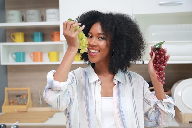 Jovem negra com cabelo afro preparando e comendo frutas antes de fazer um smoothie