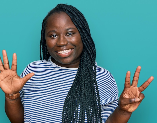 Jovem negra com tranças vestindo roupas casuais mostrando e apontando para cima com os dedos número oito enquanto sorria confiante e feliz